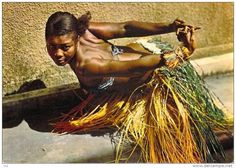 an african woman is dancing with grass on her feet and arms, in front of a wall