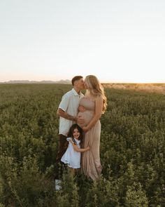 a pregnant couple and their two children are standing in the middle of a field at sunset