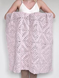 a woman holding up a pink crocheted blanket