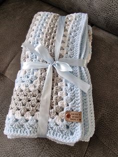 a crocheted blanket wrapped in white and blue yarn with a ribbon on top