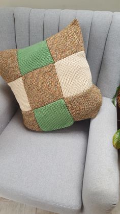 a gray chair with a green and beige pillow on it's back next to a potted plant