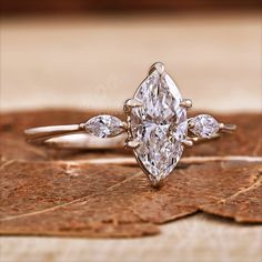 an engagement ring with three pear shaped diamonds on top of it, sitting on a leaf