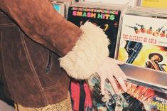 a person wearing a brown jacket and white glove holding onto a cd case filled with cds