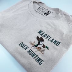 Discover the perfect shirt to capture your passion for Maryland Duck Hunting! Crafted from 100% cotton, this unisex design features a striking embroidery of the state's signature duck hunting. Get ready to show off your enthusiasm in style! Available in short sleeve, long sleeve, and crewneck 100% cotton Color is Sand Unisex Sizing Professionally Embroidered Duck Hunting, Embroidered Shirt, Perfect Shirt, Unisex Design, Maryland, Design Features, Hunting, Crew Neck, Embroidery