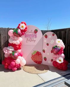 a strawberry themed birthday party with balloons and strawberries on the top, in front of a wooden fence