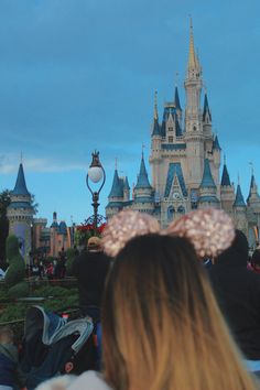 people standing in front of a castle at night with the lights on and one person wearing a minnie mouse ears headband