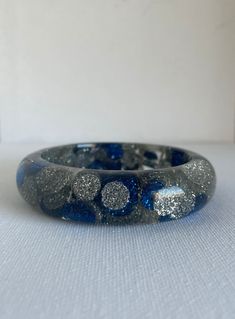 Was £35 now £27 This vintage chunky bangle is the cats meow.  With sparkly blue and silver accents that really catch the light.  This bangle can make any outfit a bit more festive.  And for me the more the merry for bangles so stack them, even have a look of you would like at all my other bangles. The condition is good for its age but the plastic is a bit cloudy to what it may had been and it does have light scratches and scuffs. Measurements: to come All sales are final so please ask any and all questions prior to purchasing. I always combine shipping at no extra cost so message me before hand and I will adjust the shipping price to show combined shipping prices.  I refund  any and all Postal overcharges if there are any. If there is something you are looking for that I do not have, feel Silver Glitter Bracelet As Gift, Silver Glitter Bracelets As A Gift, Silver Glitter Bracelets As Gifts, Adjustable Silver Glitter Bracelets, Adjustable Silver Bracelets With Glitter, Blue Glitter Jewelry For Party, Festival Accessories, Holiday Jewelry, Silver Bangle