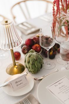 the table is set with an artichoke, wine glass, and place cards