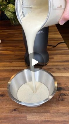 someone pouring milk into a metal bowl on top of a wooden table