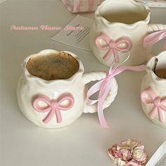 three ceramic teapots with pink bows on them sitting on a table next to an open book