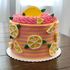 a pink and yellow striped cake with lemons on the top is sitting on a wooden table