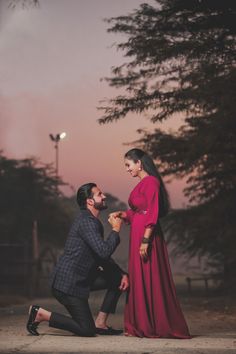 a man kneeling down next to a woman in a red dress and holding her hand