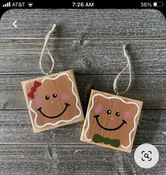 two wooden ornaments with faces on them hanging from twine strings against a wood background