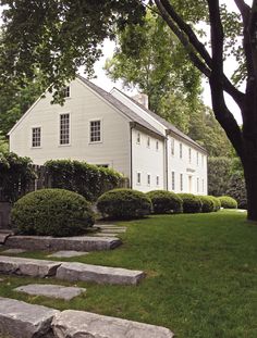 a large white house sitting on top of a lush green field next to a tree