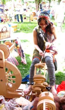 a woman sitting on top of a wooden spinning wheel in the grass next to other items