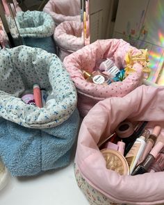 three pink and blue storage baskets filled with various makeup products on top of a white counter