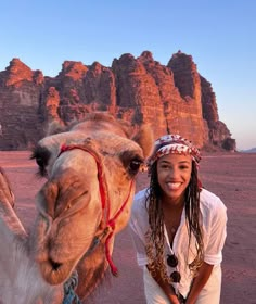 a woman standing next to a camel in the desert