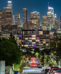 the city skyline is lit up at night, with cars parked on the street in front