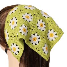 a crocheted hat with white and yellow flowers on the front, sitting on top of a mannequin's head