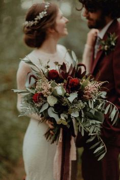 a bride and groom are standing in the woods holding their bouquets with greenery