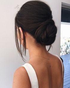 the back of a woman's head with her hair in a low bun, wearing a white tank top