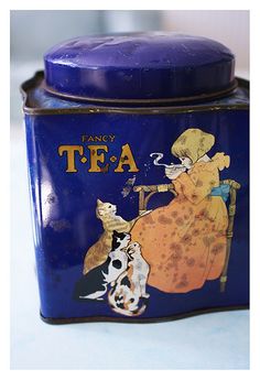 a blue tea tin with an image of a woman and dog on the lid, sitting on a table