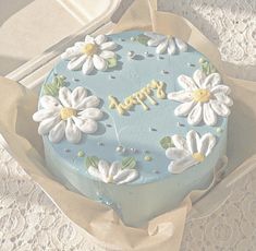 a blue cake decorated with white flowers and the words happy on it in gold lettering