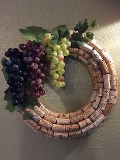 a wreath made out of wine corks with grapes hanging on the wall behind it