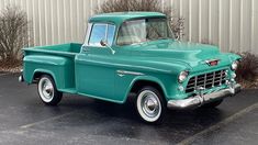 an old green pickup truck parked in a parking lot next to a white metal building