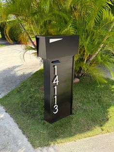 a black mailbox sitting in the grass next to a tree and sidewalk with numbers on it