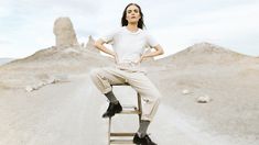 a woman sitting on top of a wooden chair in the middle of a dirt road