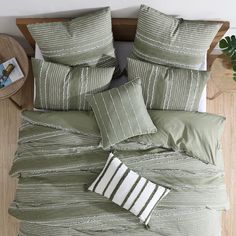 a bed with green and white comforters, pillows and blankets on top of it