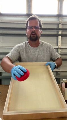 a man with blue gloves on holding a red object in front of a wooden table