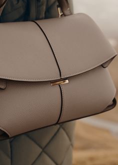 The "Mokki" model showcases the art of folding with its textured leather. The corners are cut to reveal smooth leather for a subtle interplay of textures. The bag’s interior is roomy and divided into compartments, all protected by a flap that features an engraved clasp. With its adjustable shoulder strap held in place by snap hooks, the model smoothly adapts to your movements. Luxury Beige Flap Bag, Designer Beige Leather Flap Bag, Chic Luxury Everyday Bag With Flap, Designer Taupe Top Handle Shoulder Bag, Modern Brown Satchel For Everyday Luxury, Timeless Beige Calf Leather Satchel, Luxury Structured Shoulder Bag In Calf Leather, Timeless Flap Bag For Everyday Luxury, Timeless Textured Leather Shoulder Bag For Office