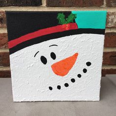 a painting of a snowman wearing a black hat and green scarf on a brick wall