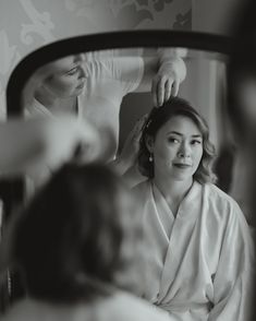 a woman is getting her hair done in front of a mirror while another person looks on