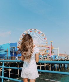 a woman standing on the edge of a pier looking at an amusement park ferris wheel