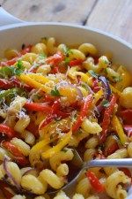 a bowl filled with pasta and vegetables on top of a wooden table next to a spoon