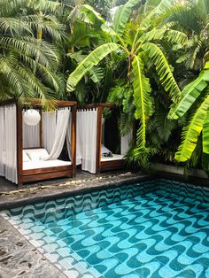 an empty pool surrounded by lush green trees and curtains on either side, with two lounge chairs facing the pool