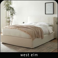 a white bed sitting on top of a wooden floor next to a potted plant