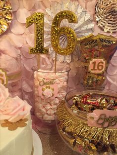 a table topped with lots of pink and gold decorations next to a cake covered in candy