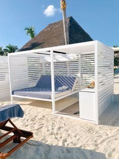 a bed sitting on top of a sandy beach next to a white building with a thatched roof