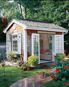 a small garden shed in the middle of a yard with flowers and plants around it