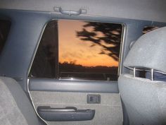 the back seat of a car with trees in the window and sunset reflected in the rear window