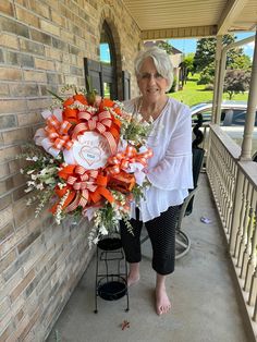 an older woman holding a bouquet of orange and white flowers in front of a brick building