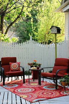 two chairs and a table on a deck with a red rug in front of it