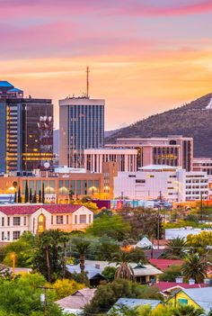 the city skyline is lit up at sunset with mountains in the background and colorful clouds