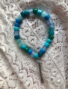 a close up of a bracelet with beads on a lace table cloth and a metal charm