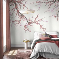 a bedroom decorated in white and pink with cherry blossoms on the wall, along with a bed