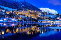 the city is lit up at night by the water and snow covered mountains are in the background